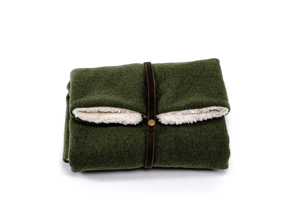 Grüne Reisedecke Forest, zusammengefaltet mit braunem Lederband, innen aus weißem, fellähnlichen Material.