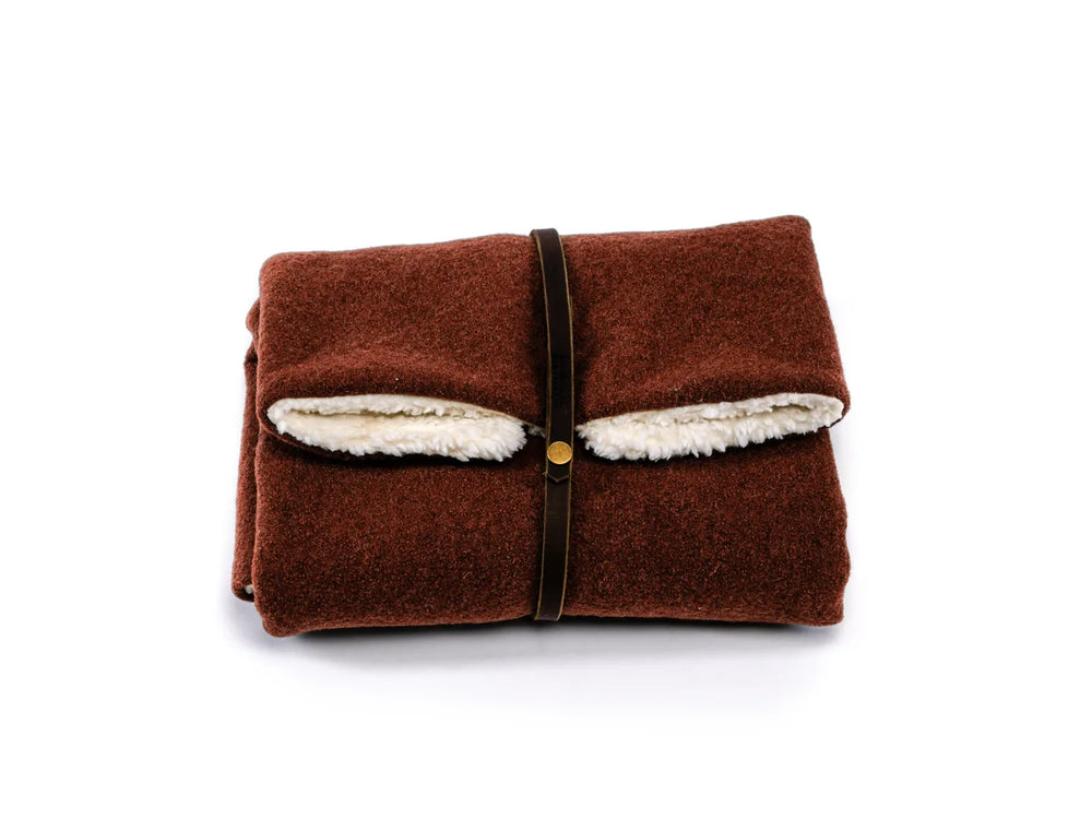 Zusammengefaltete Reisedecke Forest in warmem Braun, mit hellem Fleecematerial und braunem Lederband.