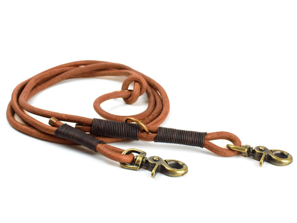 Braune doppelte Rundlederleine für Hunde mit zwei Karabinerhaken und schwarzer Griffmitte. Ideal für Spaziergänge im Freien.