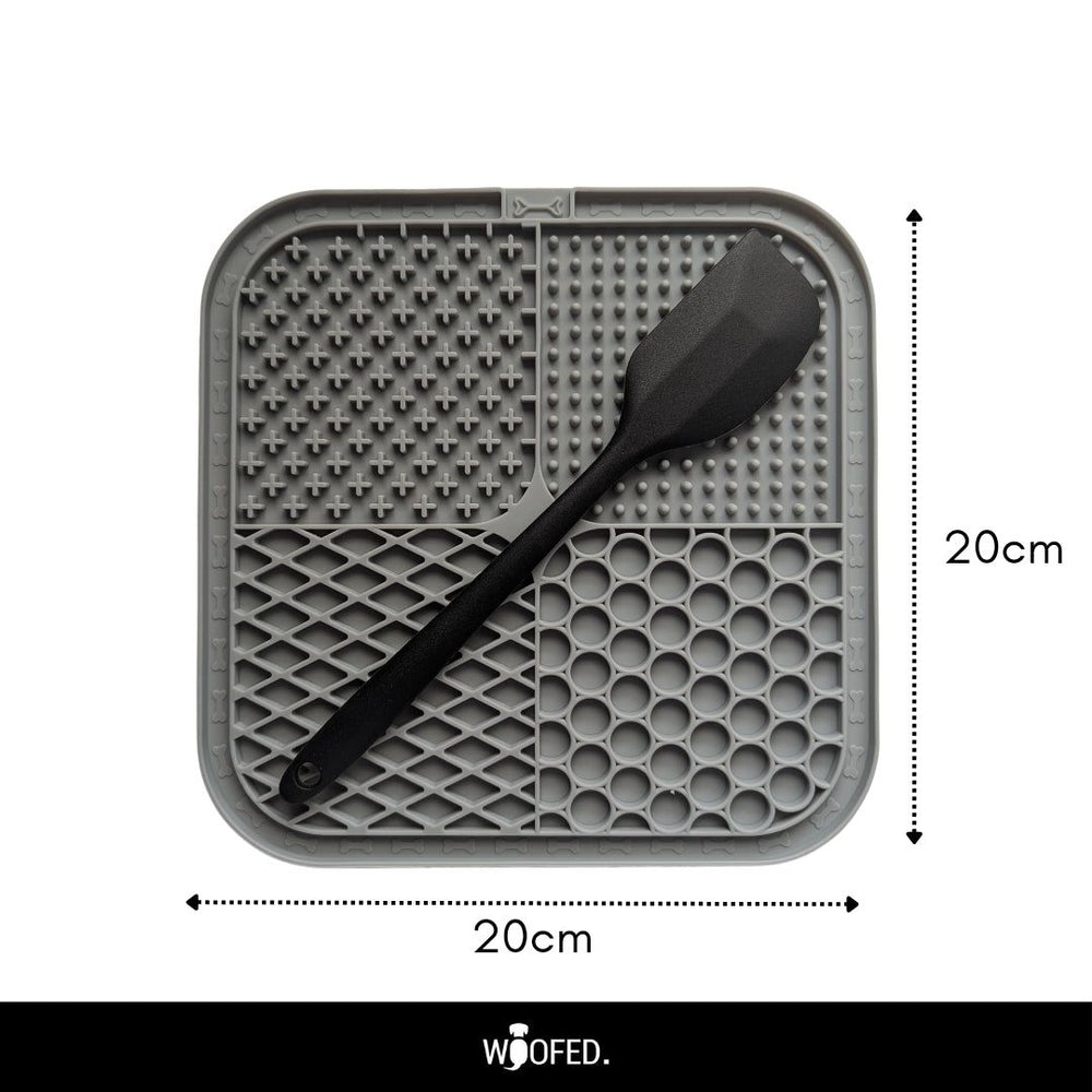 Schleckmatte aus Silikon, quadratisch (20 cm), mit strukturierten Bereichen und schwarzem Spachtel für abwechslungsreiche Snacks.