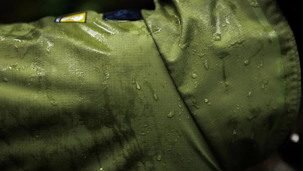 Wasserdichter, olivgrüner Sun Shower™ Coverall für Hunde mit sichtbar abperlendem Wasser.