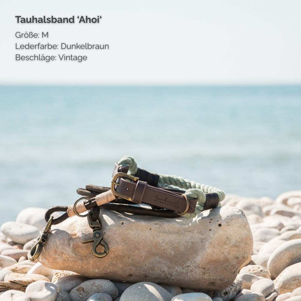 Tauhalsband Ahoi in Größe M, dunkles Leder, Vintage-Beschläge, vor maritimem Hintergrund mit Steinen am Meer.