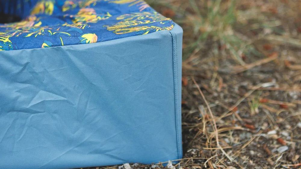 Buntes, florales Hundebett Mt. EverRest™ mit blauer Kante und gepolsterter Oberfläche in natürlicher Umgebung.