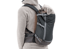 Person mit schwarzem Hunde-Rucksacktrage, in dem ein kleiner Hund sitzt, gekleidet in graue Jacke.