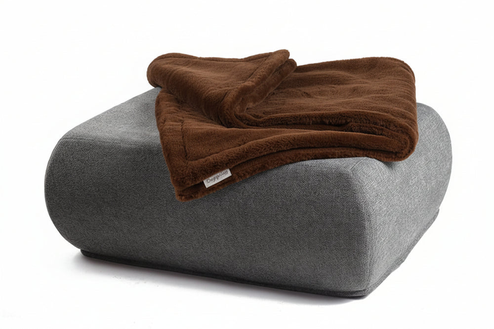 Gemütlicher Sitzpuff mit grauer Oberfläche und einer warmen, braunen Wohndecke für entspannende Atmosphäre.