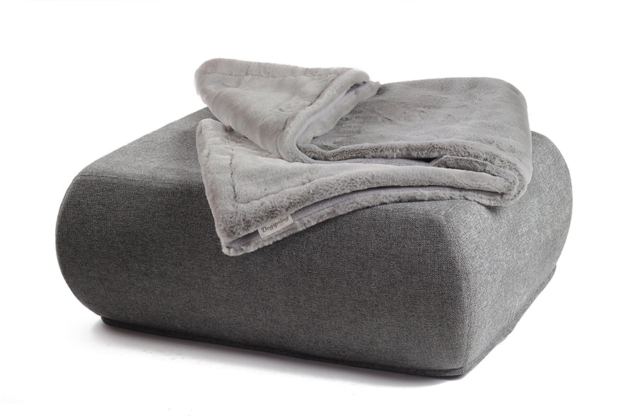 Graue Wohndecke aus Webpelz auf einem quadratischen Pouf, auf weißem Hintergrund.