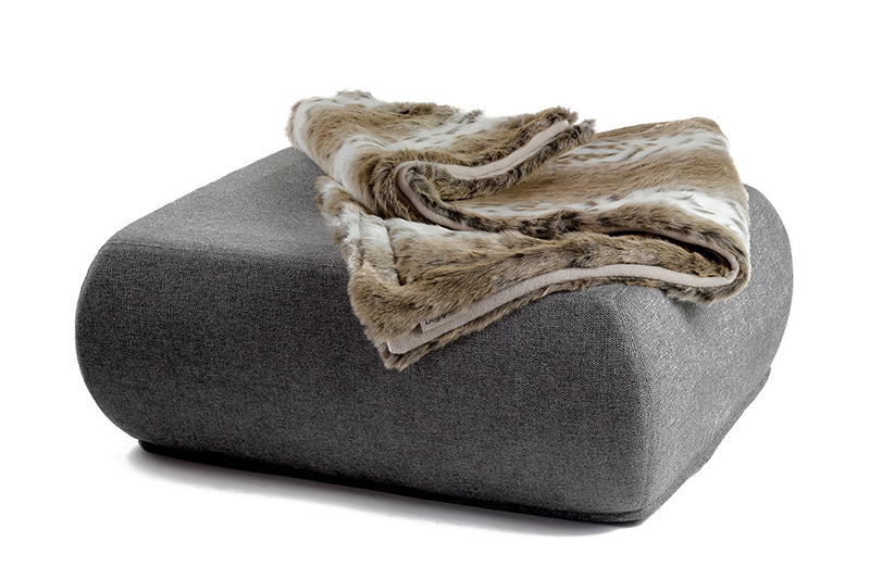 "Kuschelige Wohndecke aus Webpelz auf modernem grauen Pouf mit abgerundeten Ecken."