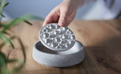 Anti-Schling Einsatz für Katzennapf: Hand hebt strukturierten Deckel über grauem Napf auf Holzuntergrund.