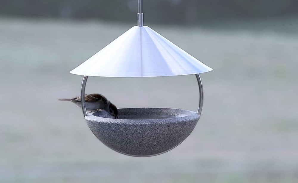 Moderner hängender Vogelfutterspender mit grauer Schüsselform und silbernem Kegeldach im Freien.