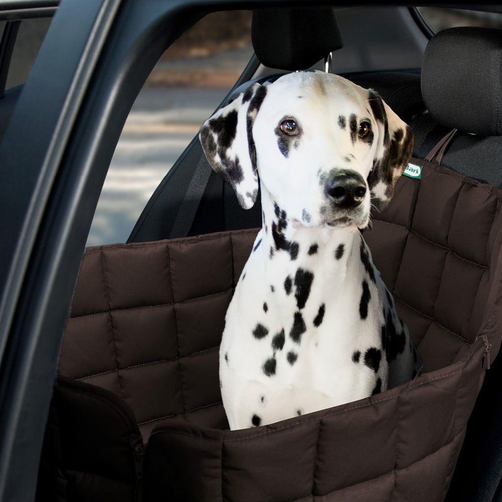 Dalmatiner sitzt in braunem, gepolstertem Autositzschutz für Hunde im Rücksitz eines Autos.