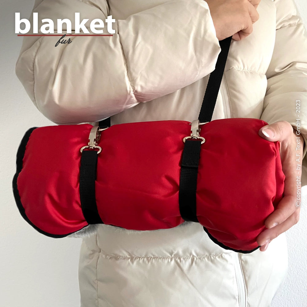 Person hält rot-schwarze Tragetasche, die wie eine zusammengerollte Decke aussieht, mit zwei schwarzen Tragegurten.