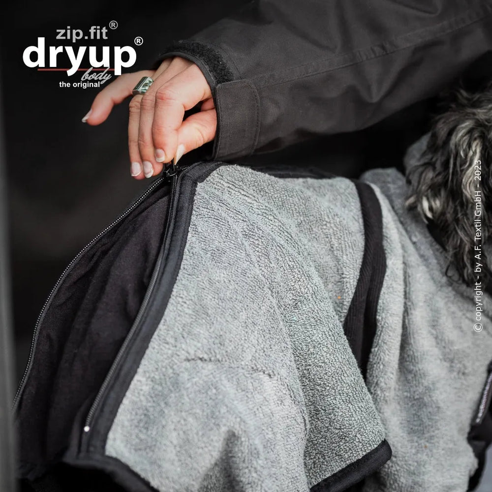 Hand zieht am Reißverschluss eines grauen Dryup® BODY zip.fit® mini Kleidungsstücks aus weichem Material.