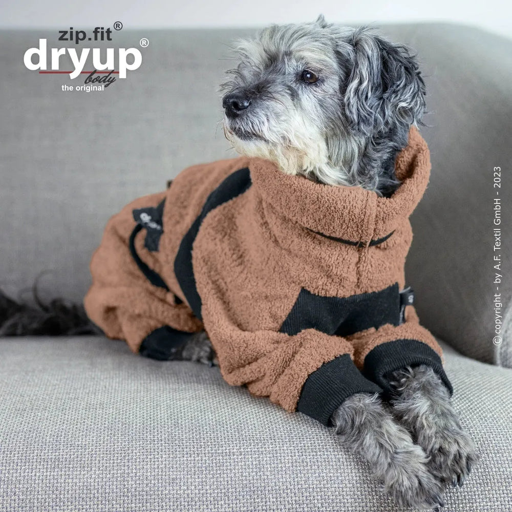 Hund im braunen fleeceartigen Overall mit hohem Kragen, entspannt auf grauem Sofa, Marke Dryup.
