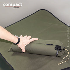 Kompakte olivgrüne Decke, zusammengerollt auf dunklem Untergrund, ideal für Regenwetter und unterwegs.