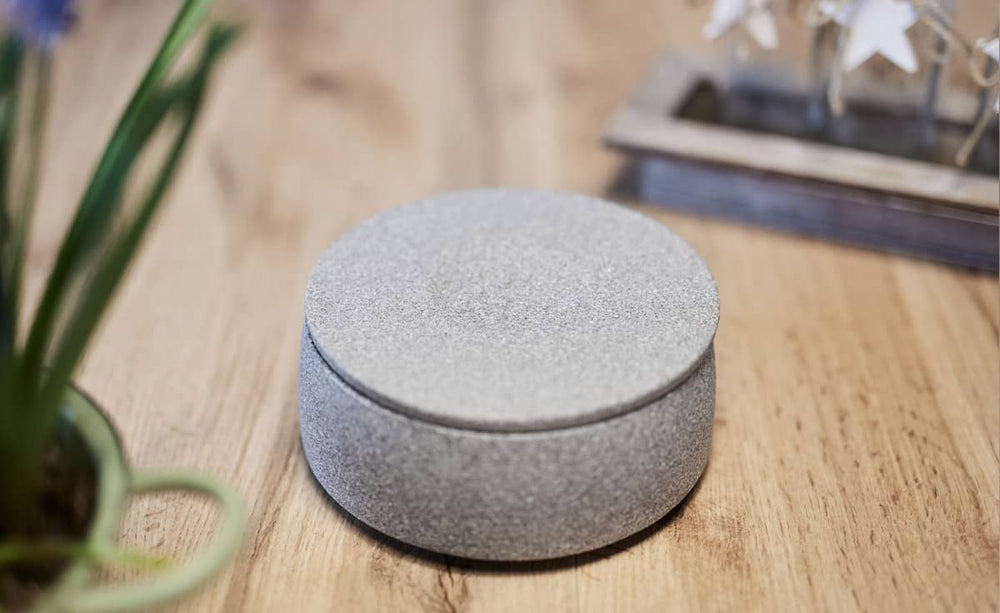 Modernes, graues Deckel für Hundenapf auf Holzoberfläche mit dekorativen Elementen im Hintergrund.