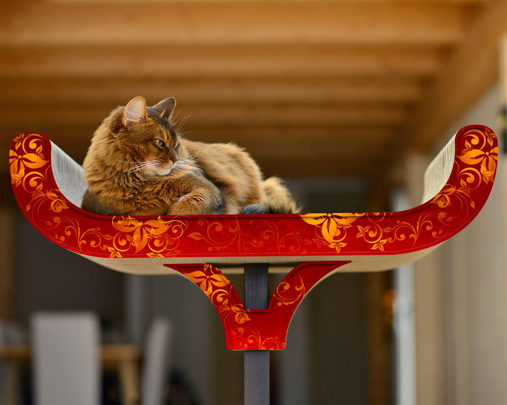 Kreativer Kratzbaum mit kunstvoll verzierten Liegen in Rot und Gold, auf dem eine entspannte Katze sitzt.
