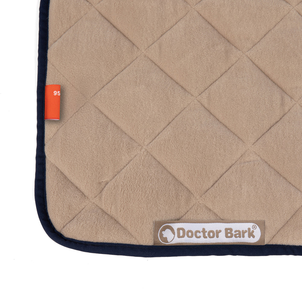 Kuschelige beige Steppdecke aus Fleece mit gestepptem Muster und orangefarbenem Etikett von Doctor Bark.