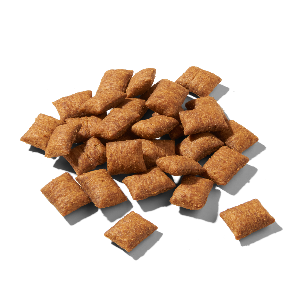 Knusprige, braune Cerealienstücke von FELIA Snacks Huhn auf schwarzem Hintergrund.