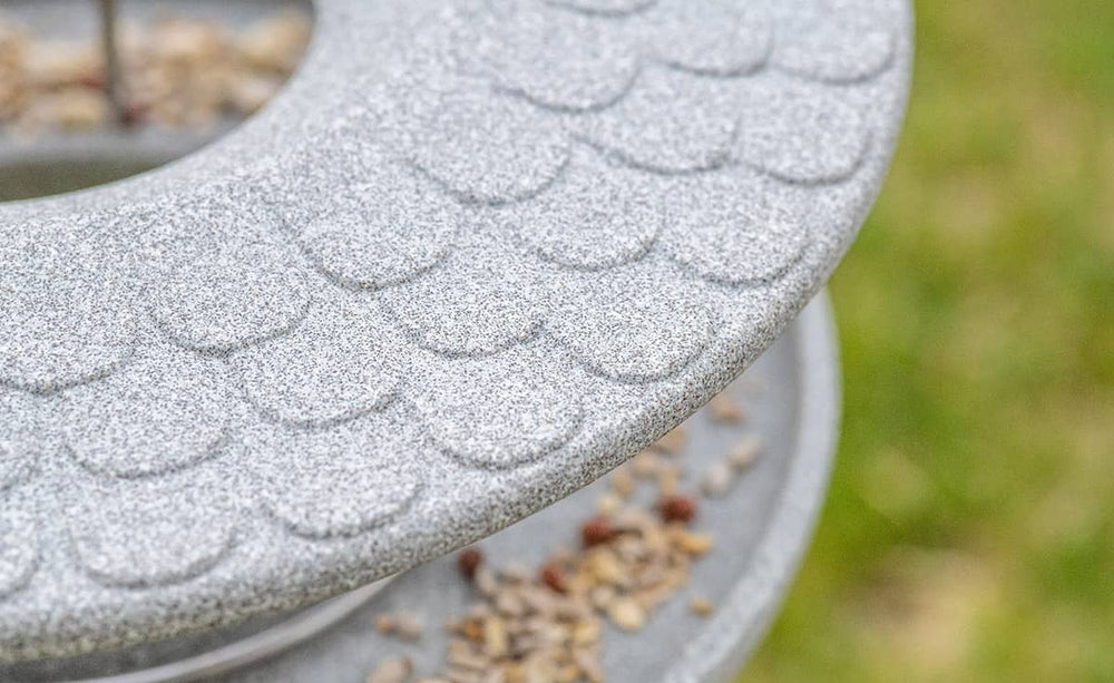 Graues Futterhaus Granicium mit Ständer und Samen auf der Plattform, vor unscharfem grünem Hintergrund.