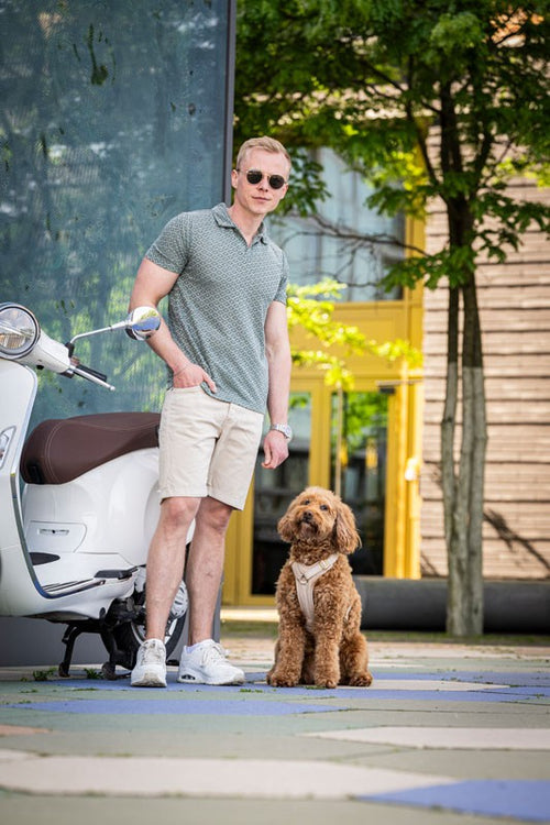 Mann mit Sonnenbrille und Hund neben einem weißen Scooter in urbaner Umgebung mit Bäumen.