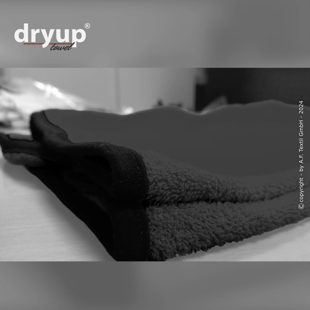 Schwarzes flauschiges Dryup® Handtuch mit fransigem Rand, ideal für hohe Saugfähigkeit, auf einer Oberfläche liegend.