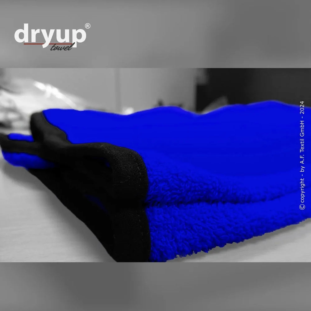 Blaues Frotteehandtuch mit schwarzen Säumen, weiche Textur und unscharfer Hintergrund, Logo "dryup" sichtbar.