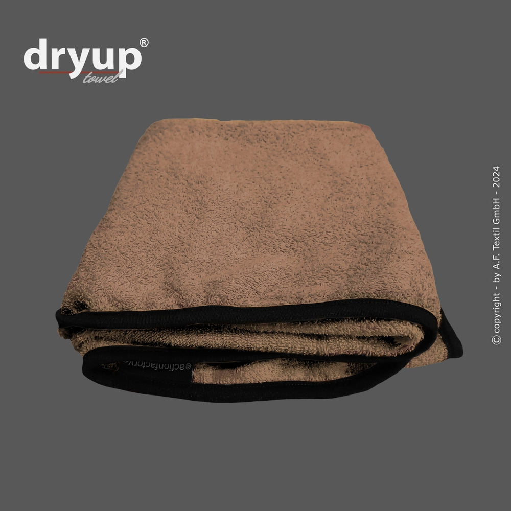 Flauschiges, gefaltetes braunes Handtuch mit schwarzen Kanten von dryup® auf hellem Hintergrund.