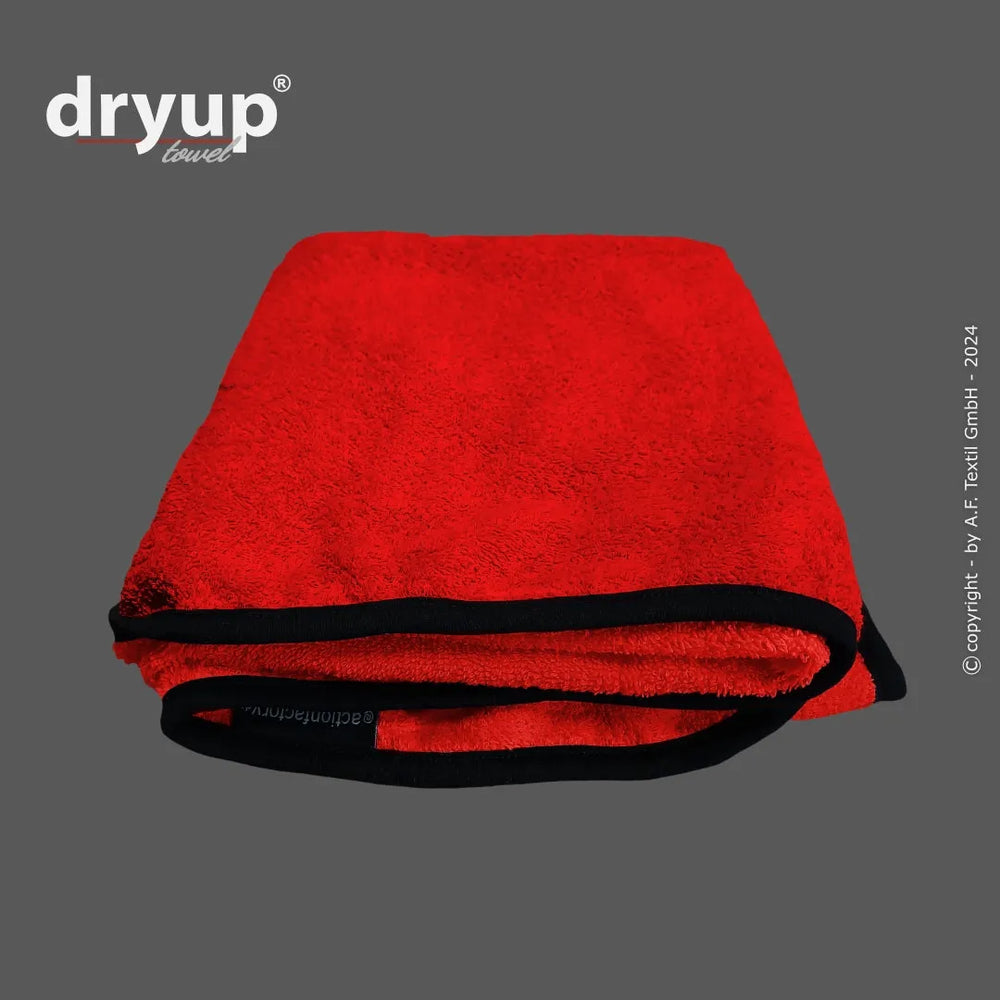Rotes Dryup® Handtuch mit schwarzem Rand auf grauem Hintergrund, weich und saugfähig. Perfekt für den täglichen Gebrauch.
