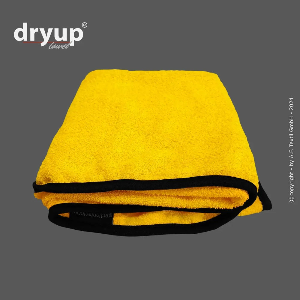 Gefaltetes gelbes Dryup® Handtuch mit schwarzem Saum, weich und saugfähig, mit Logo in der Ecke.