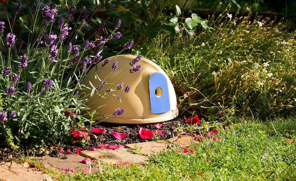 Kuppelförmiges Häuschen in beige mit blauer Tür, umgeben von blühendem Lavendel und bunten Gartenpflanzen.