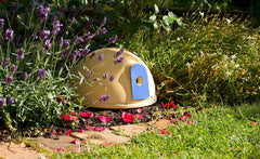 Kuppelförmiges Häuschen in beige mit blauer Tür, umgeben von blühendem Lavendel und bunten Gartenpflanzen.