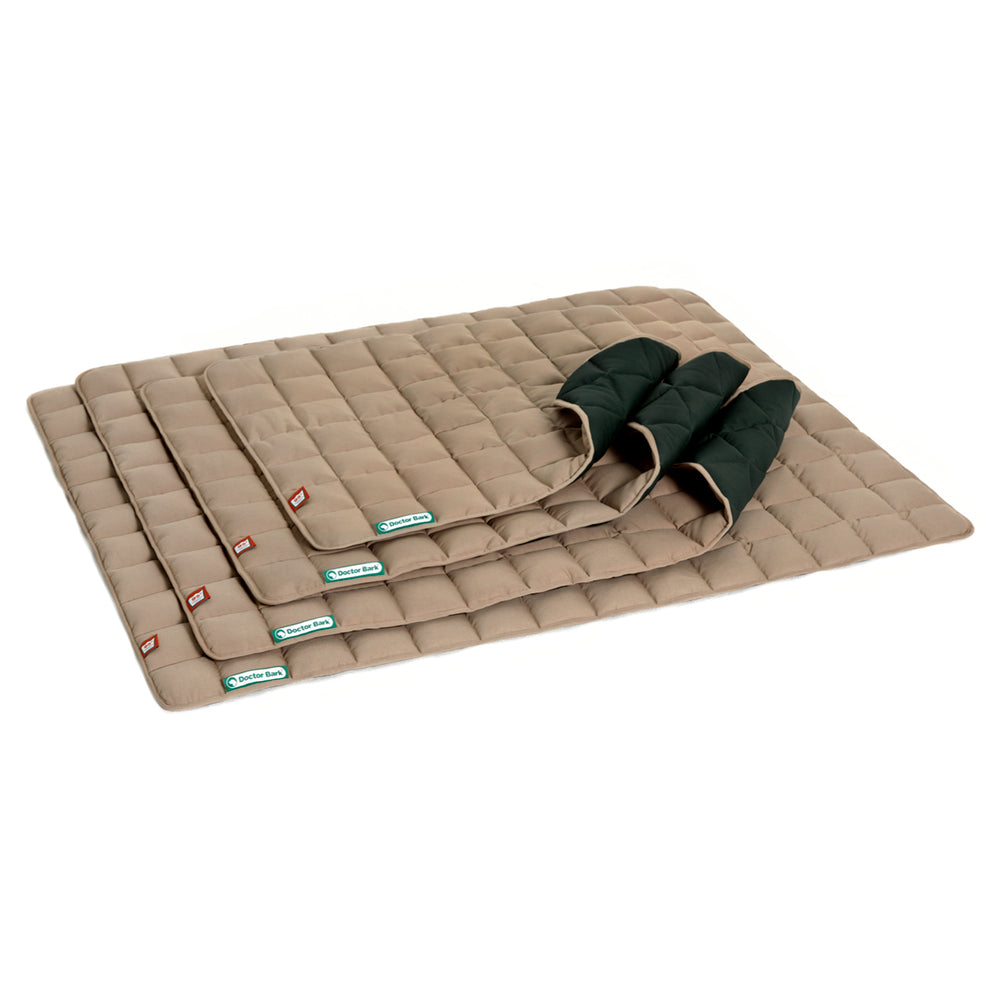 Mehrere beige Schlafunterlagen mit dunkelgrüner Griffleiste, gefaltet und in verschiedenen Größen präsentiert.