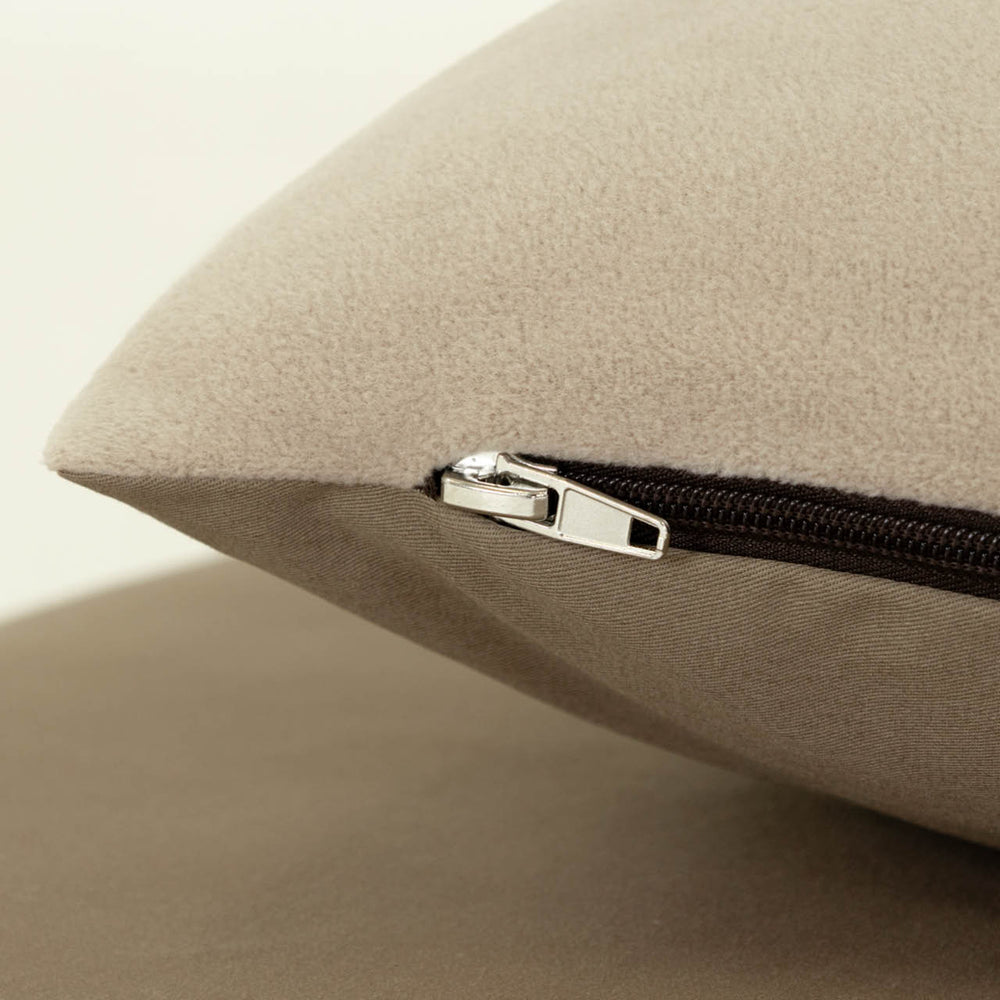 Detailaufnahme eines beige Kissenbezugs mit silbernem Reißverschluss, weicher samtiger Stoff, neutraler Hintergrund.