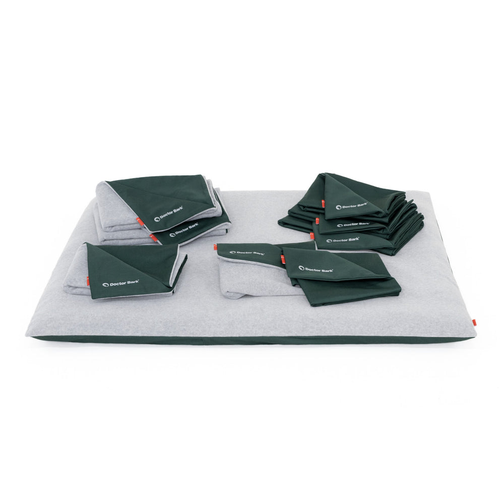 Hundebett von Doctor Bark in Grau, umgeben von gefalteten, grünen Decken mit Logo. Ideal für komfortable Tierhaltung.