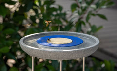 "Insektenstation Granicium mit Ständer für Bienenfutter in grauem Design, umgeben von grünen Pflanzen."