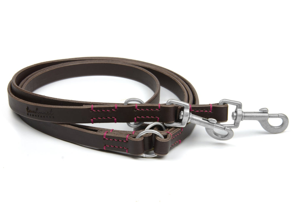 Braune Lederleine mit pinken Nähten, zwei Karabinerhaken und Ringen, hochwertig verarbeitet für Hunde.