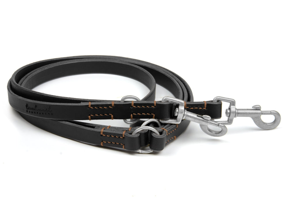 Schwarze Lederleine mit orangefarbenen Nähten und silbernen Karabinerhaken für Hunde. Robuste und stilvolle Hundeleine.