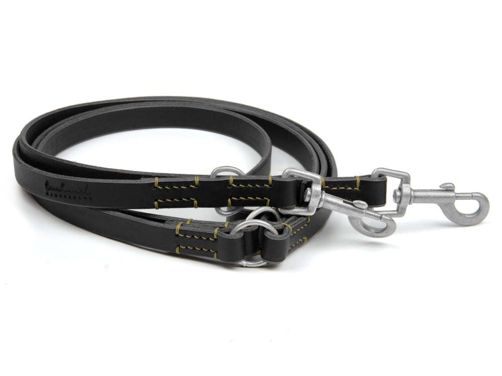 Schwarze Lederleine mit silbernen Karabinern und gelben Nähten für Hunde, robust und langlebig.