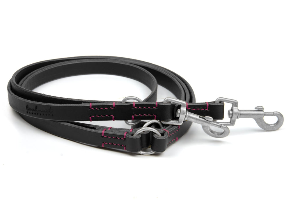 Schwarze Lederleine mit pinken Nähten, zwei Karabinerhaken und Befestigungsringen, robust und stilvoll für Hunde.
