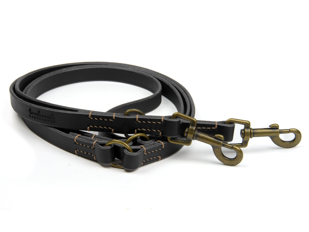 Doppelte Hundeleine aus schwarzem Leder mit braunen Nähten und zwei Karabinerhaken, ideal für Spaziergänge im Freien.