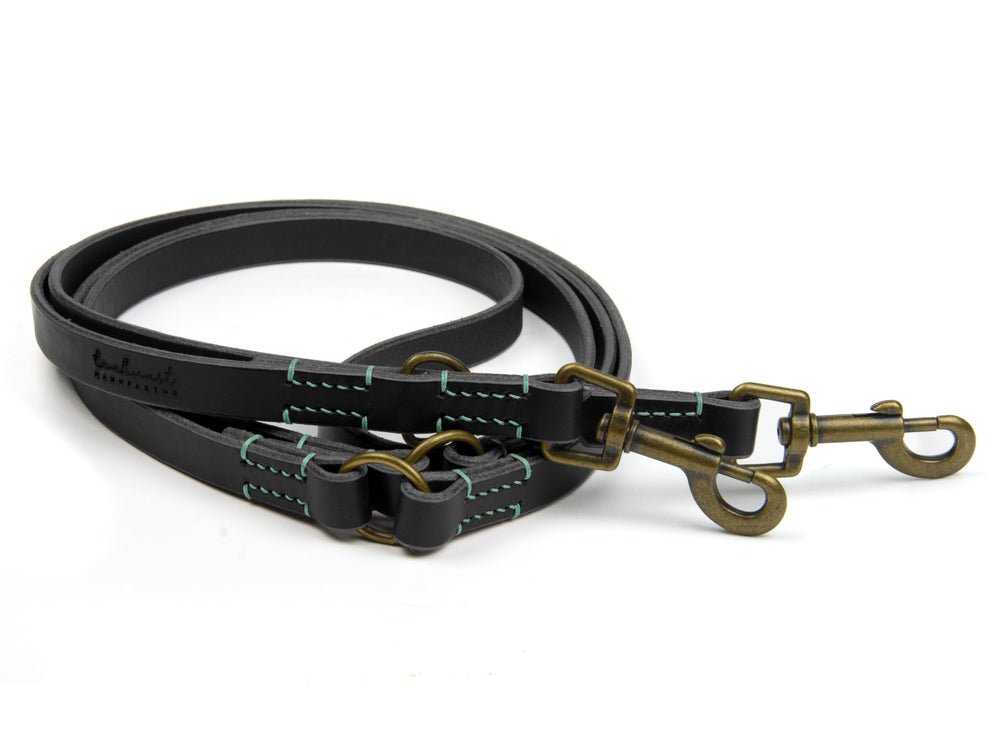 Zwei robuste Hundeleinen aus schwarzem Leder mit grüner Naht und Messingkarabinern für langlebigen Einsatz.