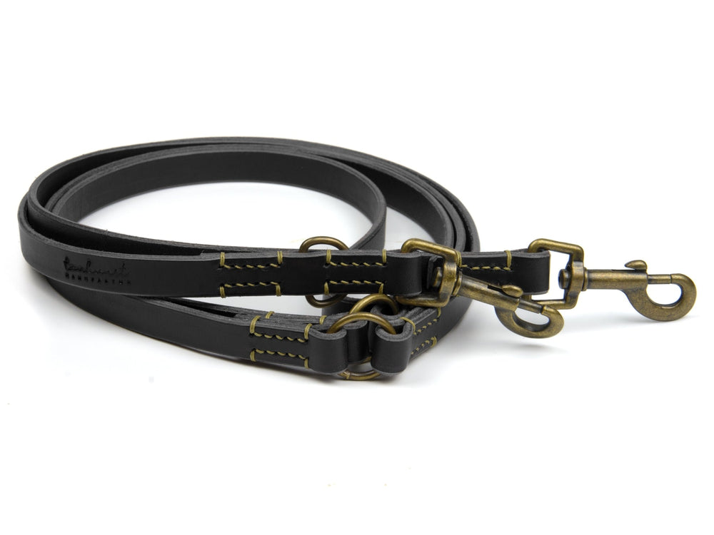 Schwarze Lederleine mit zwei Karabinern und gelben Nähten, robust und hochwertig für Spaziergänge mit dem Hund.
