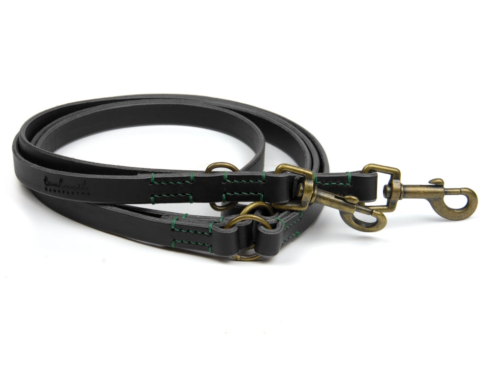 Robuste schwarze Lederleine mit grünen Nähten und messingfarbenen Beschlägen, verstellbar mit zwei Karabinerhaken.