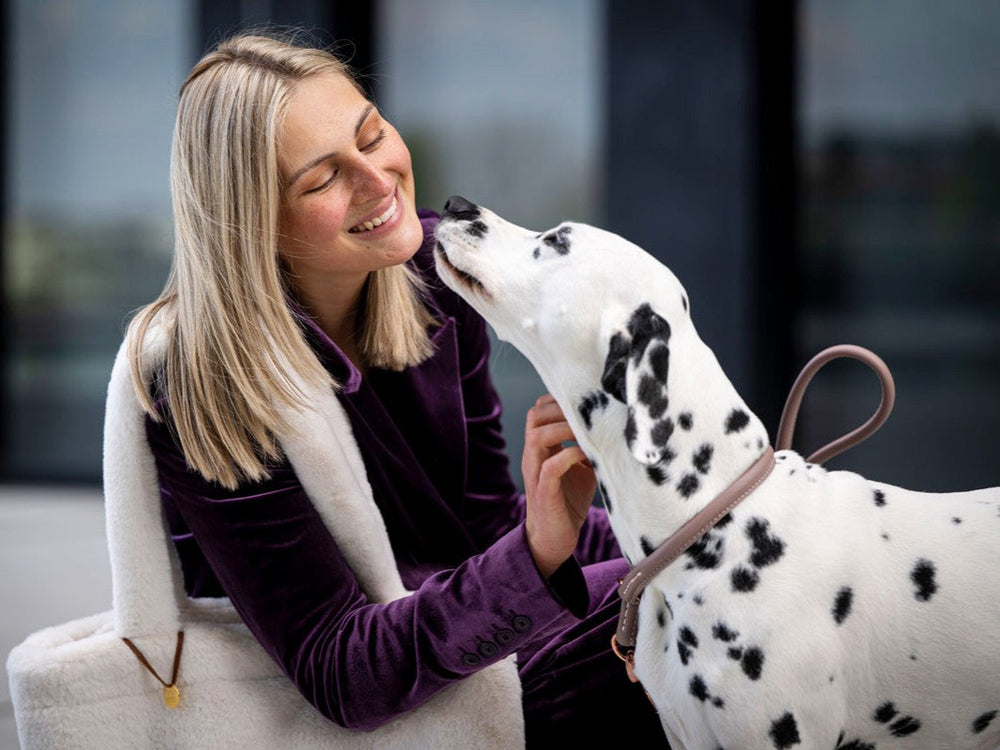 Lächelnde Frau mit blonden Haaren und Dalmatiner-Hund im lila Veloursanzug, liebevoll verbunden durch eine Leine.
