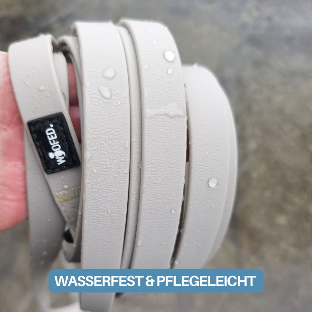 Hand mit wasserfesten Gurten der Schleppleine WOOFLEX® und Sicherheitskarabiner in neutralen Farbtönen.
