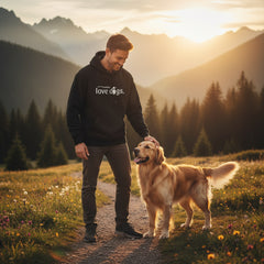 Hoodie Unisex "F*** humans love dogs" getragen von Mann mit Golden Retriever in malerischer Berglandschaft bei Sonnenuntergan