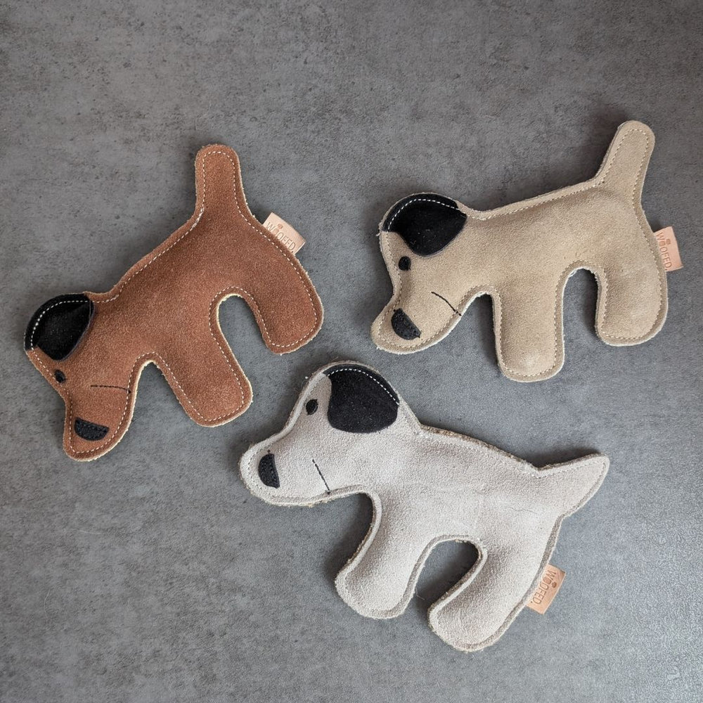 Drei farbenfrohe Hundespielzeuge aus weichem Material mit markanten Gesichtern und schwarzen Ohren auf einem neutralen Hintergrund.