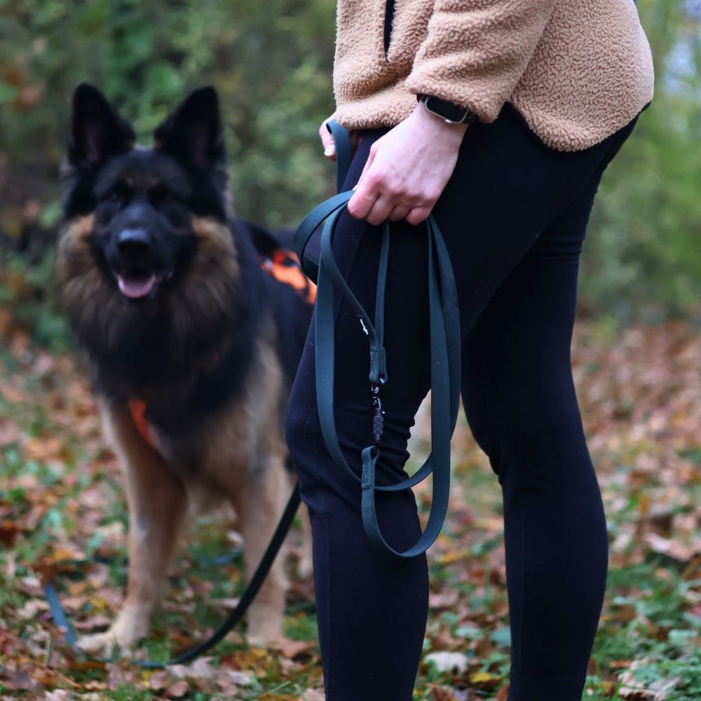 Person mit Hund an der WOOFLEX® Schleppleine auf einem Waldweg, Deutscher Schäferhund neben ihr.