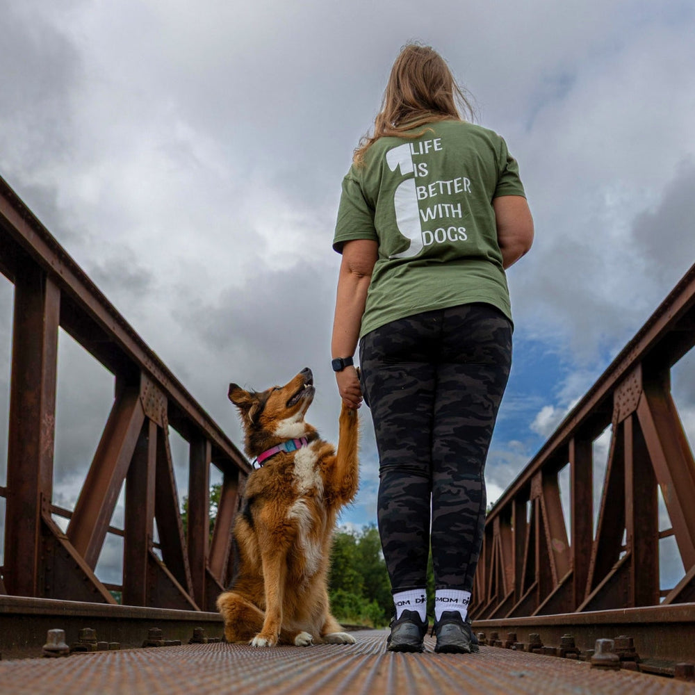 Person mit langem Haar in grünem T-Shirt "Life is better with dogs" hält Hundepfote im Hintergrund.