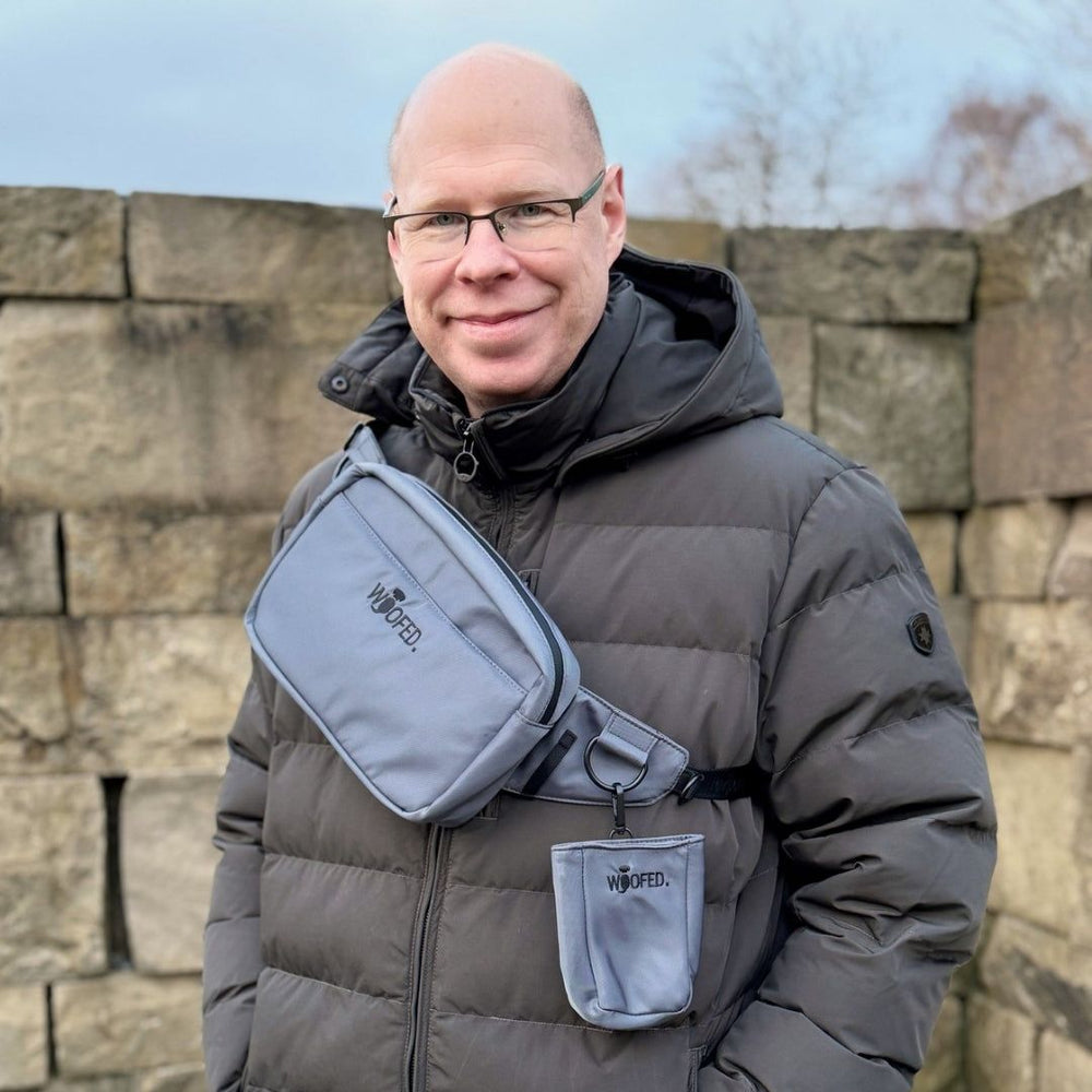 Mann mit grauem Wintermantel trägt graue WOOFED Gürteltasche vor Steinfelwand, ideal als Bauchtasche oder Schultertasche.
